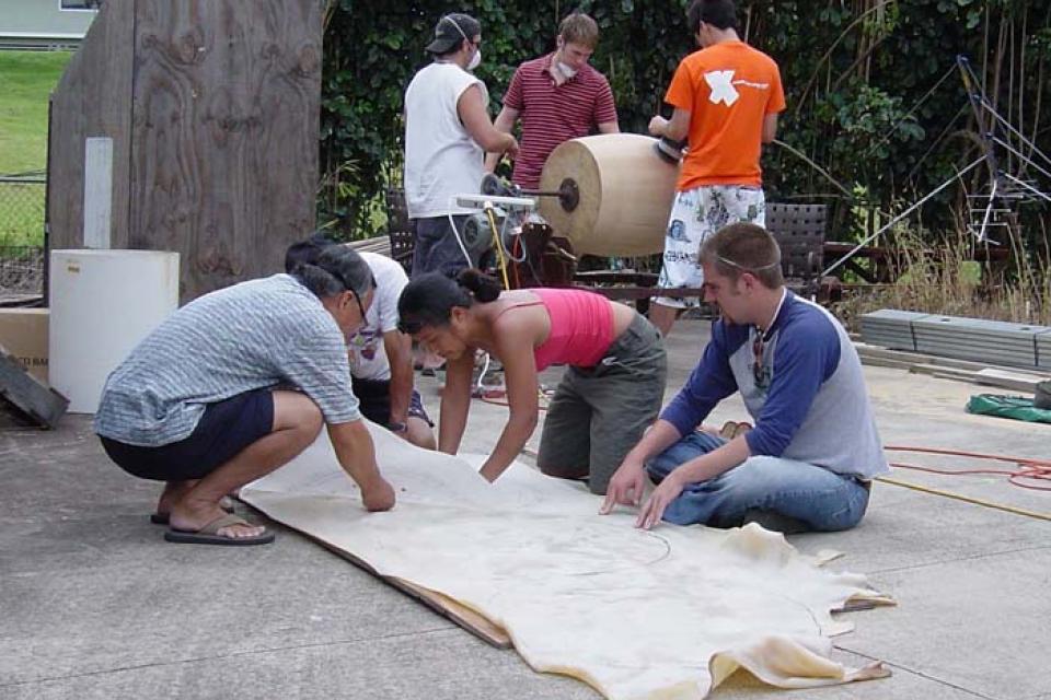 Three taiko members crouched around a skin while three other members sand a barrel in the background